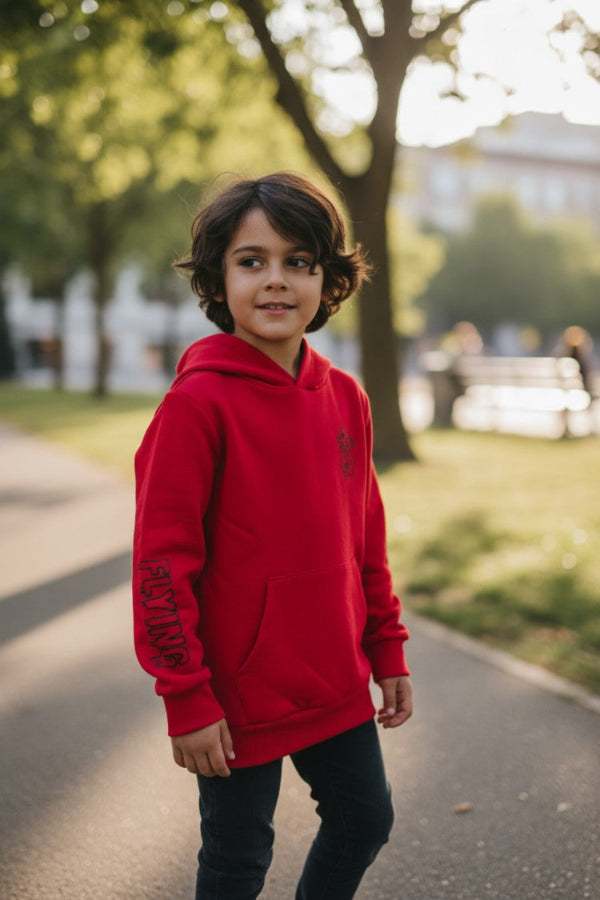 Child wearing a red hoodie standing on a path with trees and grass in the background FLYING THEM